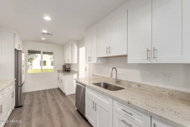 a kitchen with a sink dishwasher and white cabinets with wooden floor