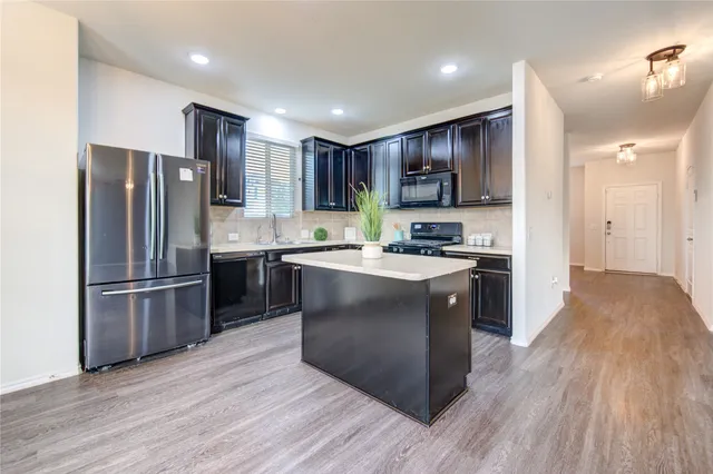 a kitchen with stainless steel appliances granite countertop a refrigerator a sink dishwasher a stove and a oven with wooden floor