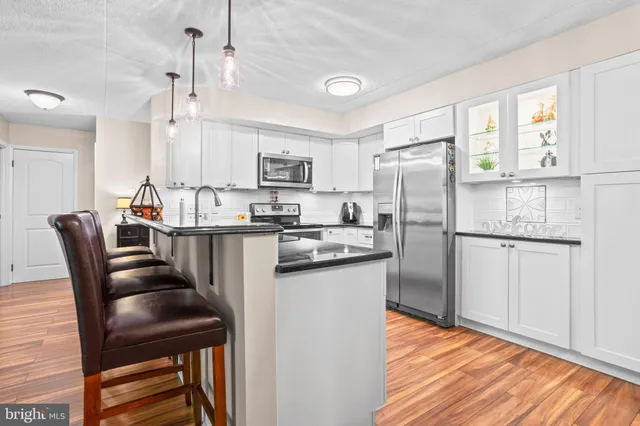 a kitchen with stainless steel appliances granite countertop a stove top oven a sink a refrigerator white cabinets and wooden floor