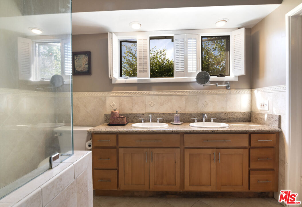 9527 Oakmore Road Los Angeles, CA 90035 - Photo 19 of 29 a bathroom with a granite countertop sink a large mirror and a bathtub