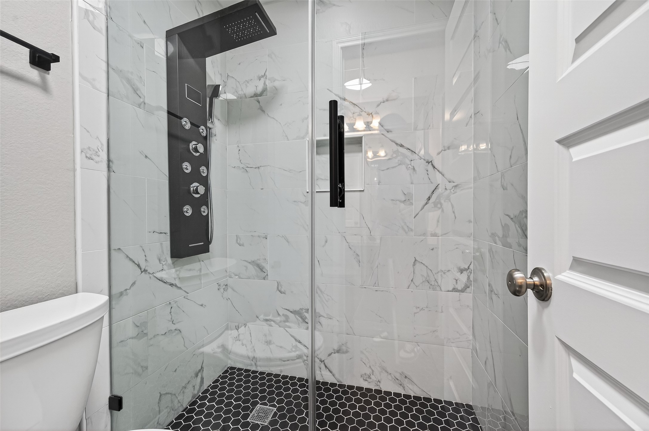 7003 Bristol Memorial Drive Spring, TX 77379 - Photo 34 of 40 Updated shower located within the Jack-and-Jill bathroom in this Spring TX 77379 home, featuring full-height marble-look tile surround and a modern glass enclosure. The black hex tile flooring adds contrast and contemporary style, while the upgraded multi-function shower panel enhances everyday convenience. Clean lines and neutral finishes create a polished, move-in ready feel in this well-designed secondary bath