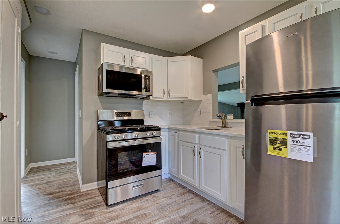14507 Glencliffe Road Cleveland, OH 44111 - Photo 11 of 31 Kitchen with tasteful backsplash, white cabinetry, light wood-type flooring, appliances with stainless steel finishes, and sink