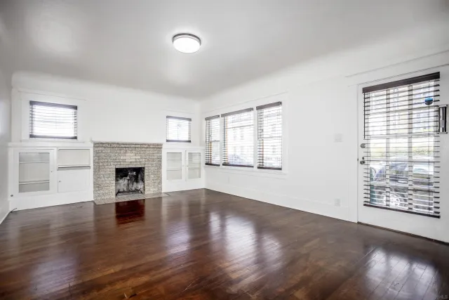 an empty room with wooden floor fireplace and windows