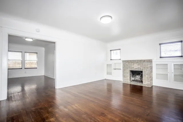 an empty room with wooden floor fireplace and windows