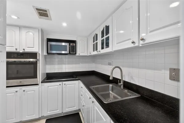 a kitchen with granite countertop a sink and a stove top oven with white cabinets