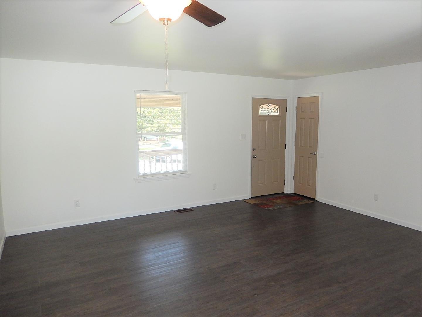 an empty room with wooden floor cabinet and windows