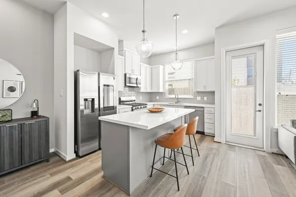 a kitchen with stainless steel appliances granite countertop a refrigerator a sink dishwasher a stove and a dining table with wooden floor