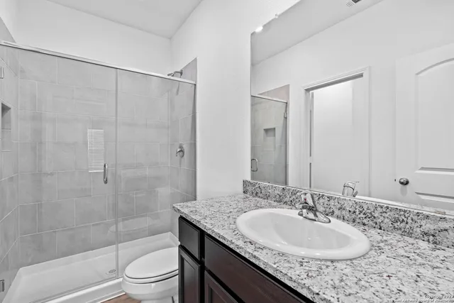 a bathroom with a granite countertop sink a toilet a mirror and shower