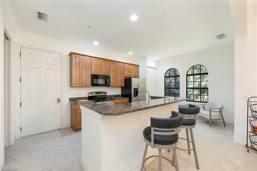 9145 Chula Vista Street, Unit 13004 Naples, FL 34113 - Photo 5 of 24 a kitchen with stainless steel appliances granite countertop a stove top oven a sink dishwasher and white cabinets with wooden floor