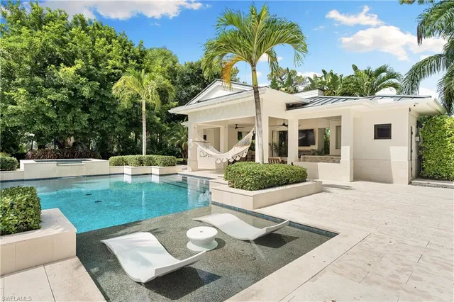 a view of a white house with a yard plants and a lawn chair