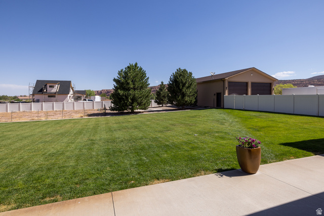 4635 East Sunny Acres Lane Moab, UT 84532 - Photo 23 of 56 Expansive green lawn with mature evergreen trees, a concrete patio, and a detached two-car garage with roll-up doors