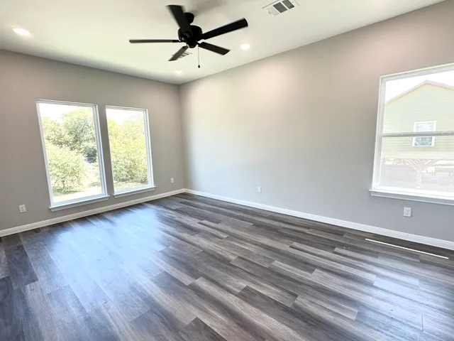 an empty room with wooden floor fan and windows