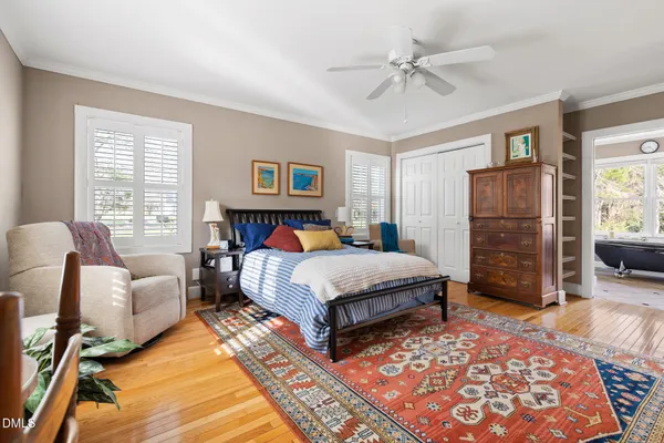 a spacious bedroom with a bed a table and a dresser with wooden floor