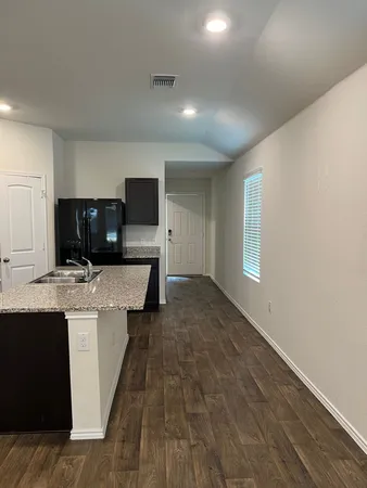 a living room with stainless steel appliances kitchen island granite countertop a sink and a stove top oven with wooden floor