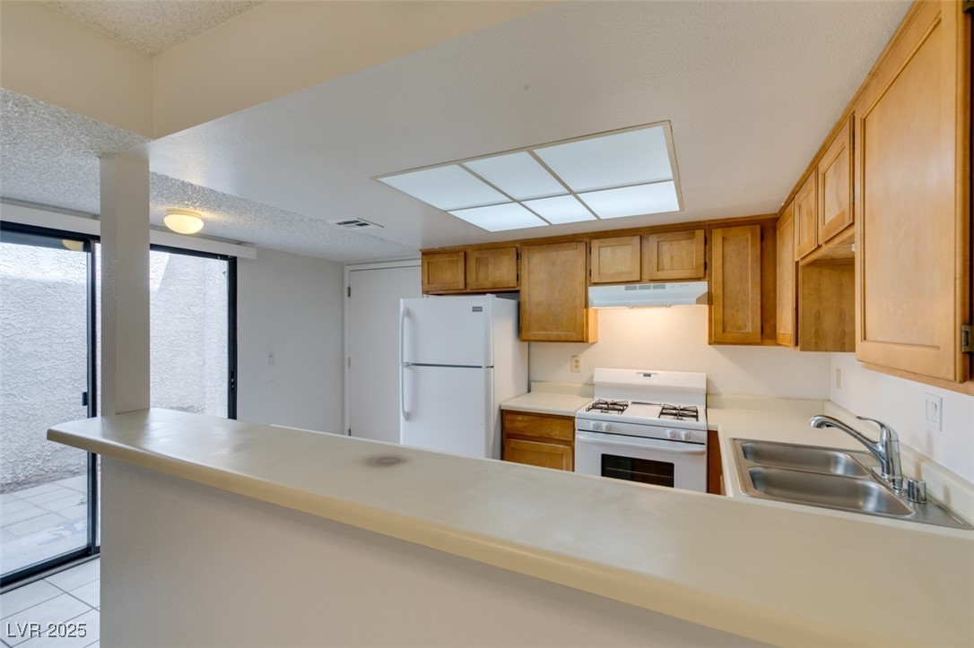 2681 Ruthe Duarte Avenue Las Vegas, NV 89121 - Photo 21 of 43 Kitchen with a sink, light countertops, white appliances, a peninsula, and under cabinet range hood