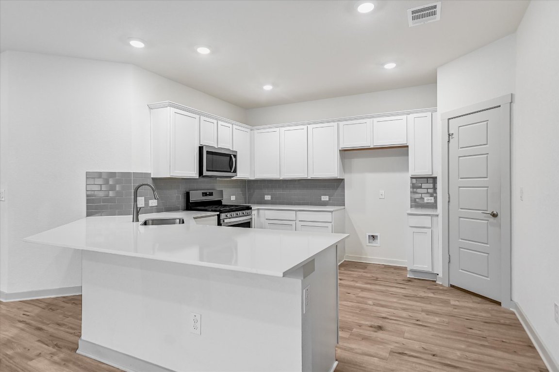 Beautiful white themed kitchen with Silestone countertops, chic grey subway tile backsplash, white cabinets, stainless steel appliances (gas range, microwave, dishwasher), pantry, wood look vinyl plank flooring, breakfast bar, & recessed lighting.