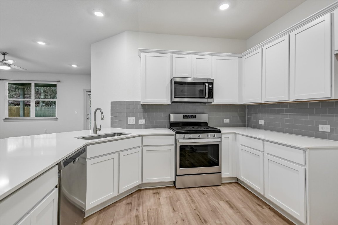 132 Shawii Pass Leander, TX 78641 - Photo 5 of 35 Beautiful white themed kitchen with Silestone countertops, chic grey subway tile backsplash, white cabinets, stainless steel appliances (gas range, microwave, dishwasher), pantry, wood look vinyl plank flooring, breakfast bar, & recessed lighting.