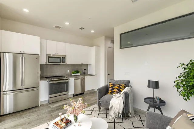 a kitchen with stainless steel appliances kitchen island granite countertop a refrigerator a stove a sink dishwasher and white cabinets with wooden floor