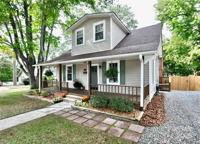 a view of a white house with a small yard and large tree and plants