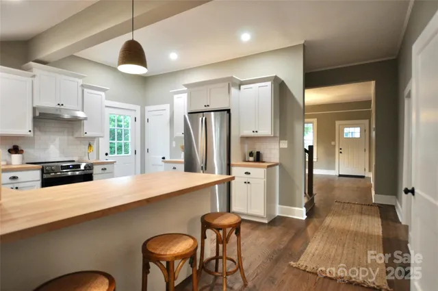 a kitchen with stainless steel appliances a refrigerator a sink a stove and chairs with wooden floor