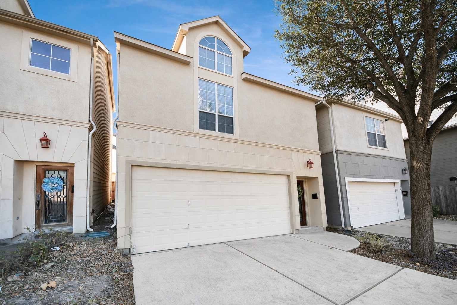 Beautiful townhouse with a clean, modern exterior featuring a large arched window, two-car garage and spacious driveway.