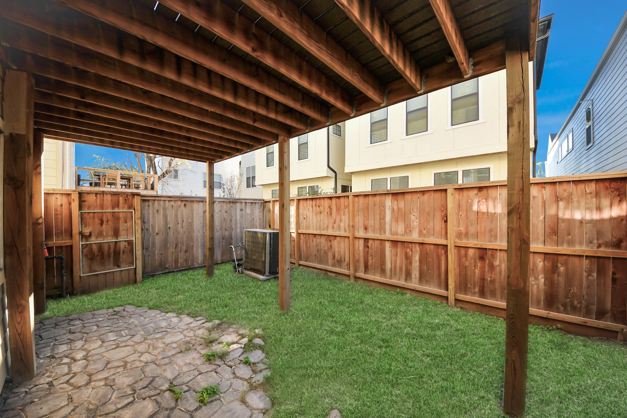 5909 Katy Street Houston, TX 77007 - Photo 30 of 34 Covered backyard area with a wooden fence, grassy lawn, and a stone patio. It offers a private, shaded space ideal for outdoor activities or relaxation.