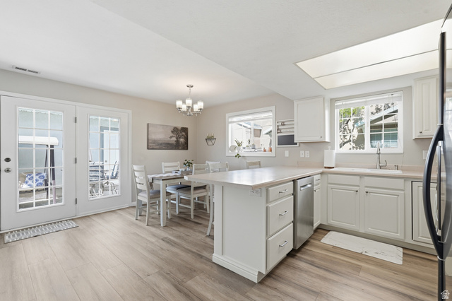 99 Penhurst Place Logan, UT 84341 - Photo 8 of 34 Bright kitchen and dining area featuring light wood-finish flooring, white cabinetry, a built-in stainless steel dishwasher, and a large window above the sink