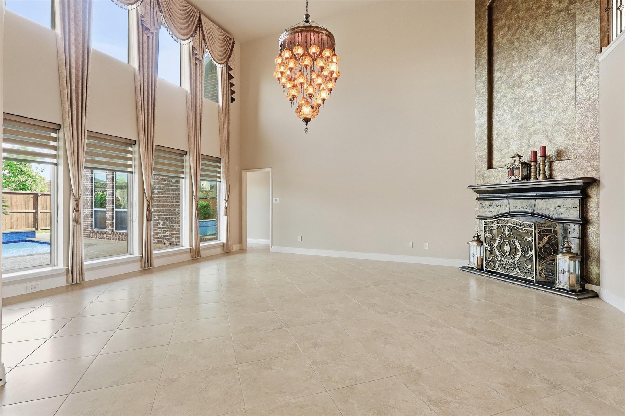 4130 Clover Ridge Lane Sugar Land, TX 77479 - Photo 5 of 48 This elegant living space features a high ceiling with a grand chandelier, large windows with drapes offering abundant natural light and a view of the outdoor pool. The ornate fireplace and neutral tile flooring add a touch of luxury.