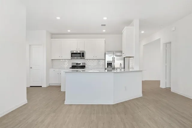 a view of kitchen with stainless steel appliances granite countertop a stove a sink a refrigerator and white cabinets with wooden floor