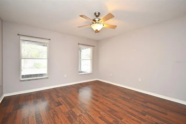 an empty room with wooden floor chandelier fan and windows