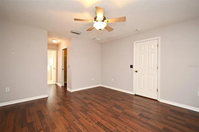 an empty room with wooden floor and fan
