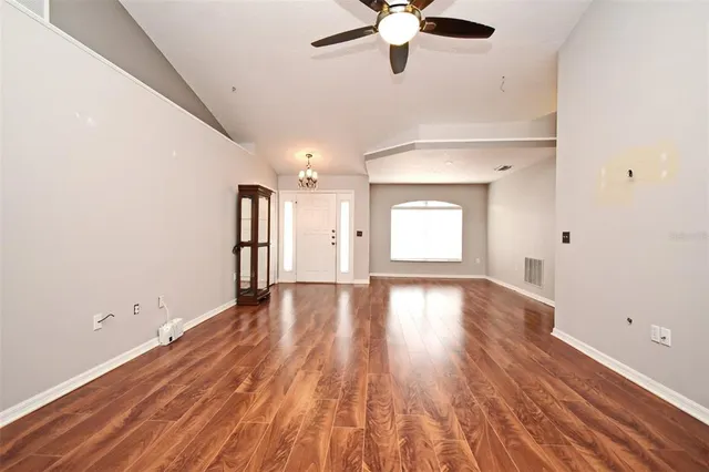 an empty room with wooden floor chandelier fan and windows
