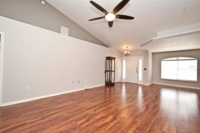 an empty room with wooden floor chandelier fan and windows
