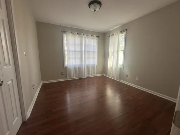 an empty room with wooden floor and windows with curtains