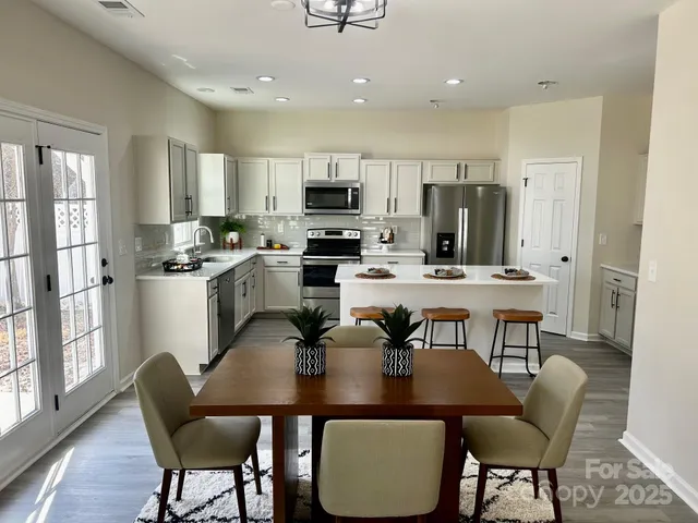 a kitchen with stainless steel appliances granite countertop a dining table chairs refrigerator and microwave