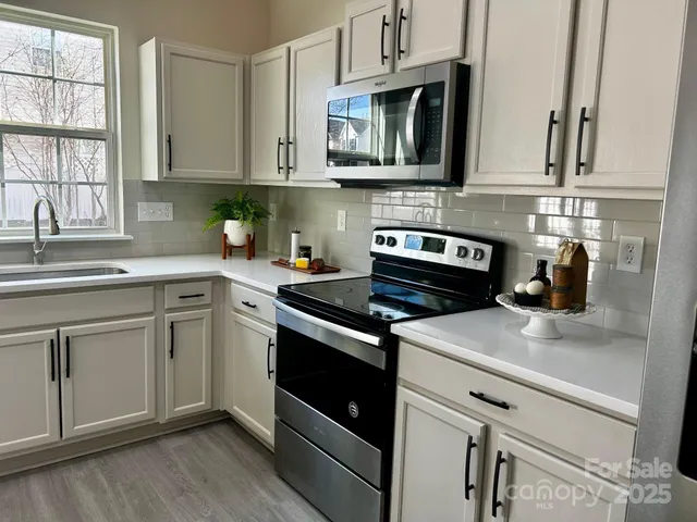 a kitchen with stainless steel appliances granite countertop white cabinets a sink and dishwasher a stove with wooden floor