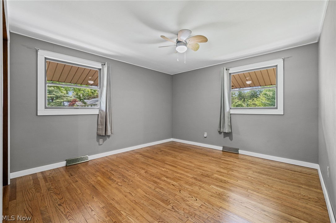 17583 Shurmer Road Strongsville, OH 44136 - Photo 31 of 50 Room featuring hardwood flooring, two windows, a ceiling fan with integrated lighting, gray wall paint, and white trim