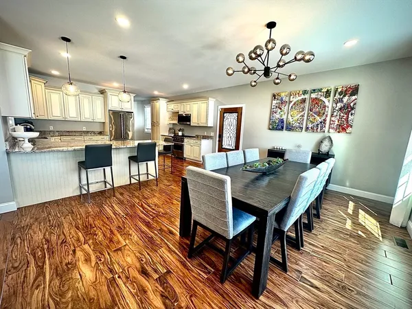 a kitchen with stainless steel appliances granite countertop a refrigerator a sink dishwasher a dining table and chairs with wooden floor