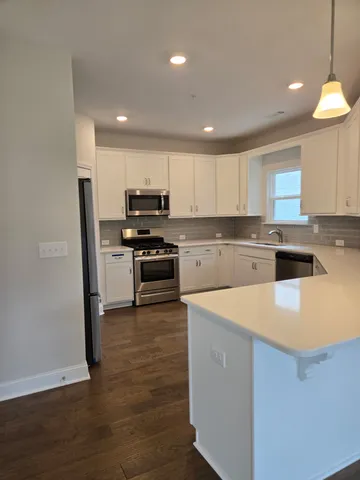 a kitchen with stainless steel appliances granite countertop a stove a refrigerator a sink a microwave and white cabinets with wooden floor