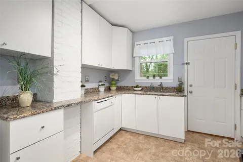 a kitchen with granite countertop white cabinets white appliances a sink and a window
