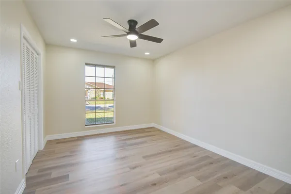 an empty room with wooden floor fan and windows