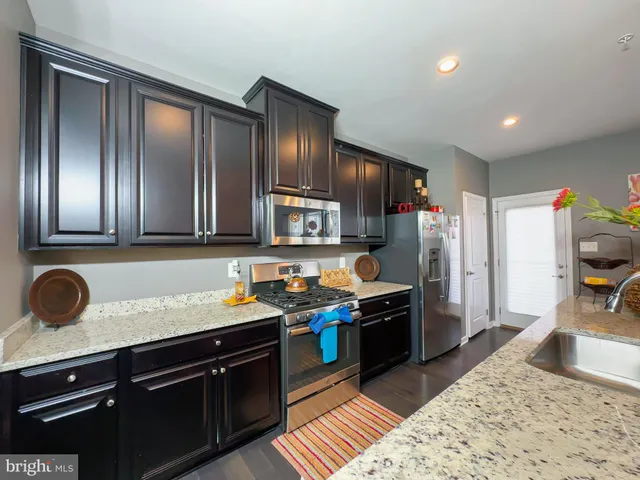 a kitchen with granite countertop stainless steel appliances a sink stove refrigerator and cabinets