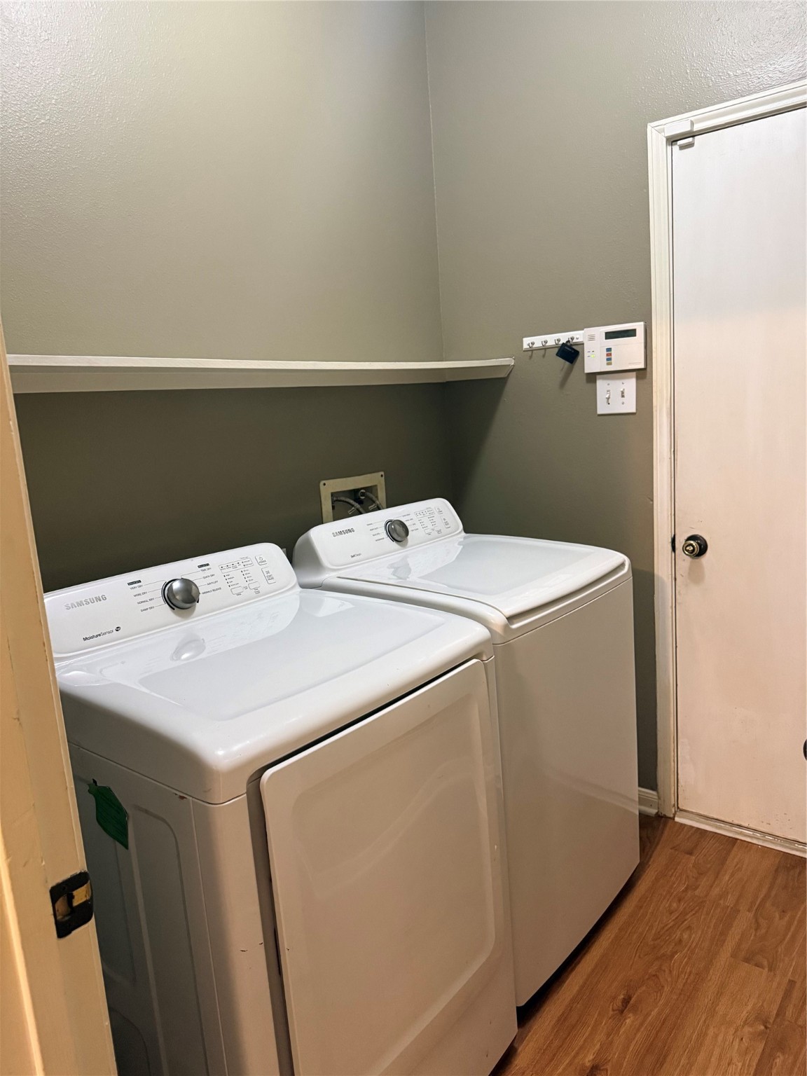 915 Saginaw Bay Court Spring, TX 77373 - Photo 13 of 15 This photo shows a laundry room featuring a washer and dryer set against a neutral-colored wall. There's a shelf above for storage, and the space has wood-look flooring.