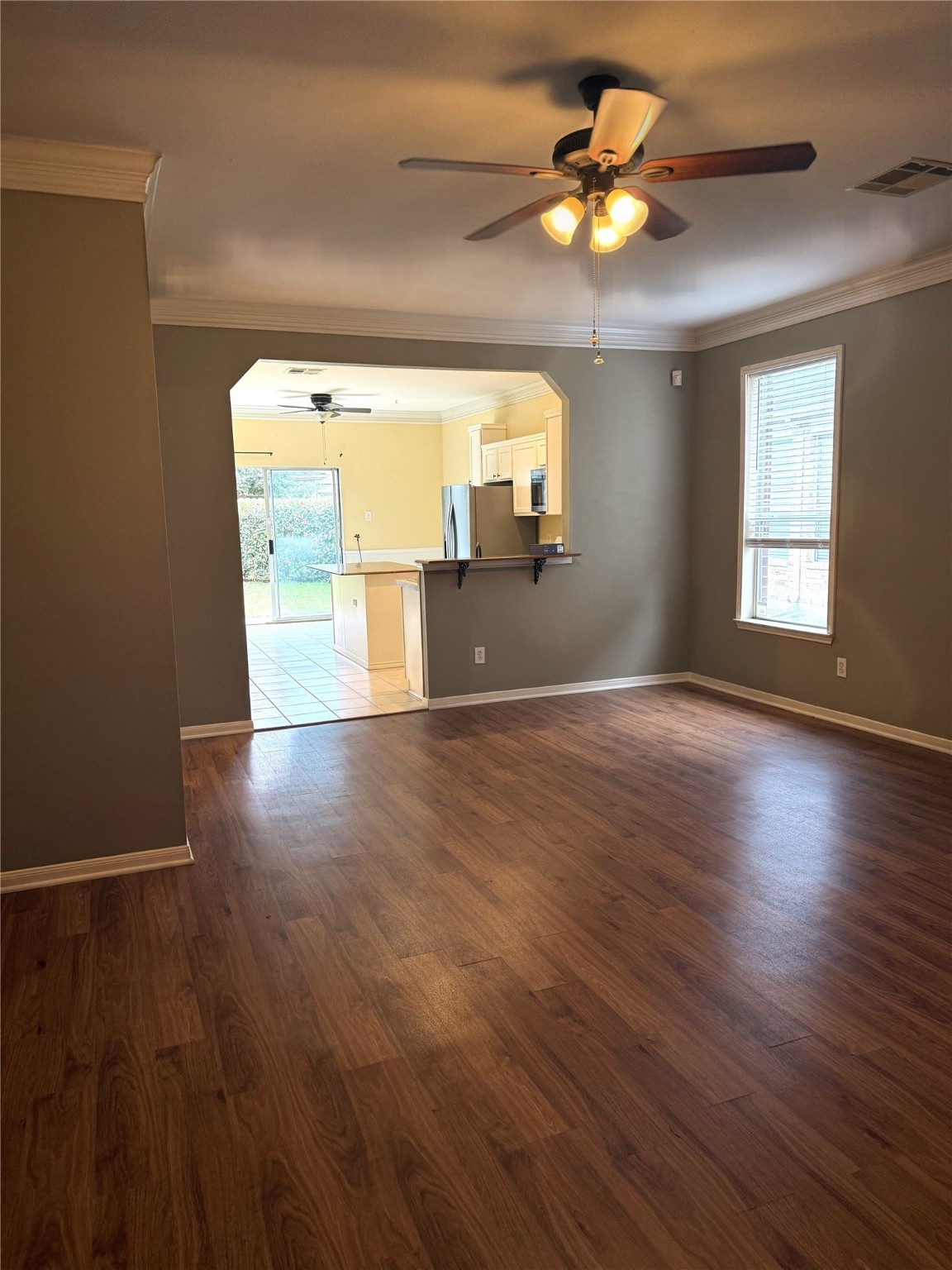 915 Saginaw Bay Court Spring, TX 77373 - Photo 5 of 15 This photo features a cozy living area with Vinyl flooring, neutral walls, and a ceiling fan. It opens into a bright kitchen with tile flooring and stainless steel appliances, leading to the backyard view through sliding doors. Natural light fills the space through large windows.