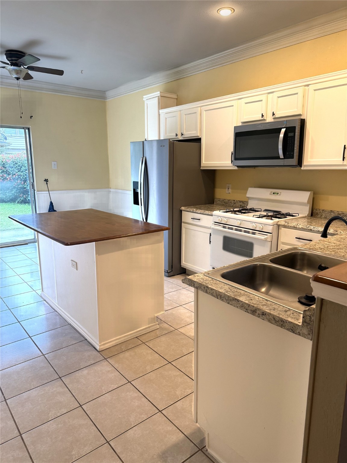 915 Saginaw Bay Court Spring, TX 77373 - Photo 8 of 15 Bright, open kitchen with modern appliances, tile flooring, and a central island. Features a ceiling fan and sliding glass door leading to the backyard, enhancing natural light.