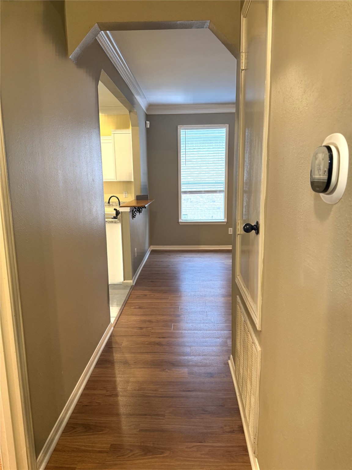 915 Saginaw Bay Court Spring, TX 77373 - Photo 9 of 15 This photo shows a hallway with warm-toned walls and vinyl flooring. It leads to a bright room with a window, and a glimpse of a kitchen area with a sink and cabinets is visible on the left.