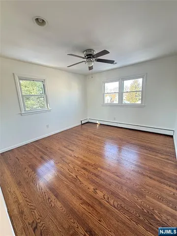 an empty room with wooden floor ceiling fan and windows