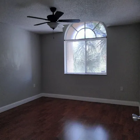 an empty room with wooden floor chandelier fan and windows
