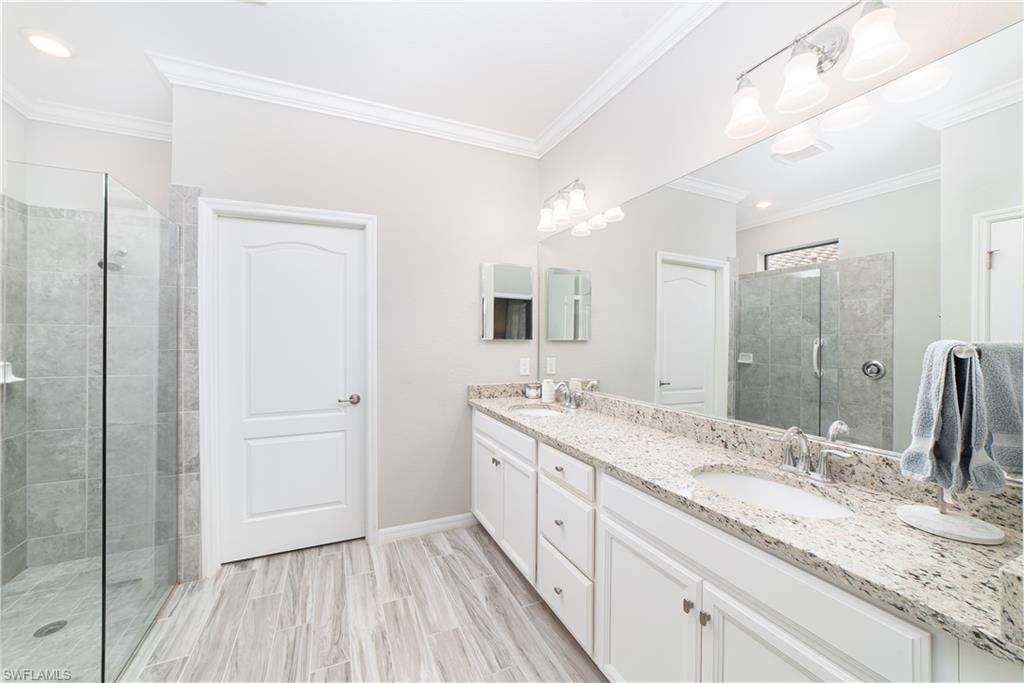 1654 Marton Court Naples, FL 34113 - Photo 8 of 29 Primary bath, dual sinks in vanity, glass shower enclosure, linen closet and custom walk-in closet are featured.