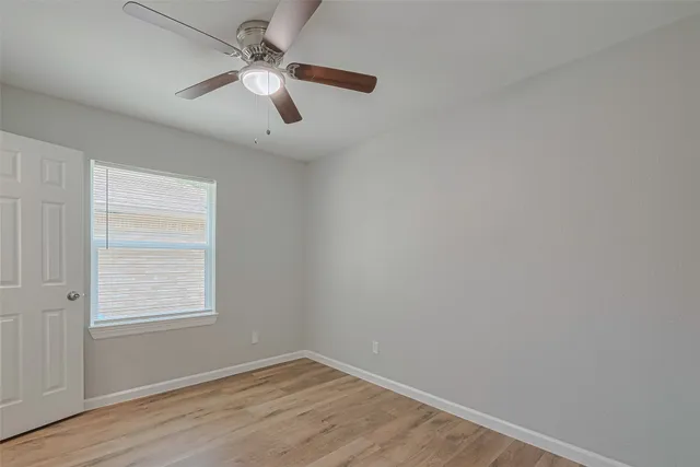 an empty room with wooden floor chandelier fan and windows